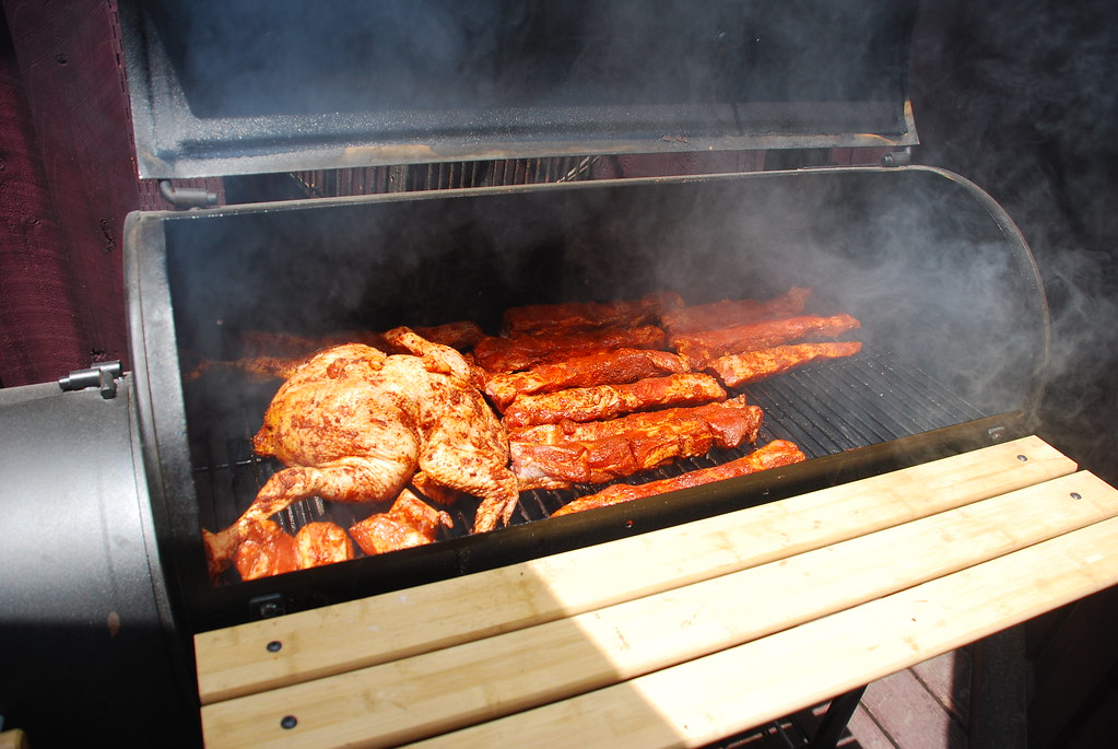 Meat being grilled on a professional barbecue smoker with thick white smoke
